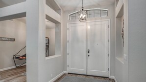 A hallway with a double door, a hanging light fixture, and a basketball hoop in the background.