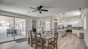 A spacious kitchen with white cabinets, a large island, and a dining area with wooden chairs and a glass table.