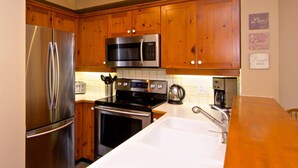 A kitchen with wooden cabinets, stainless steel appliances, a microwave, a toaster, and a coffee maker. - Upper Benchlands :Great townhouse, corner unit in quiet Treeline. Ski in/ ski out shuttle steps away (Whistler)