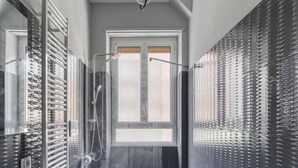 A modern bathroom with a large bathtub, a walk-in shower, and a window providing natural light. - SAPIENZA Grand Apartment (ROMA)