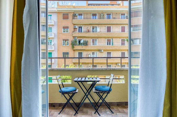 Un balcon avec une table et deux chaises, donnant sur une rangée d’immeubles d’habitation.