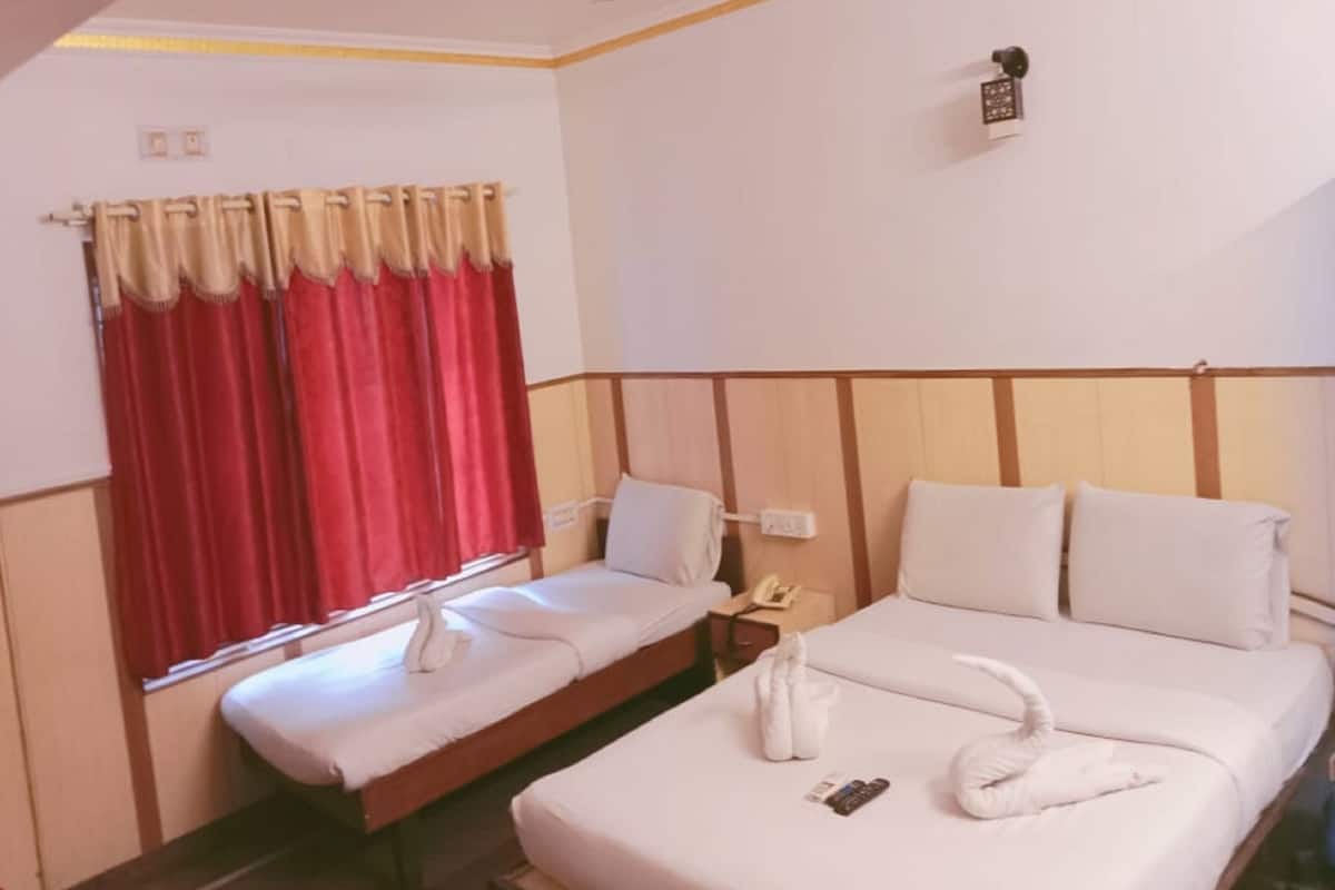 Hotellihuone, jossa on kaksi sänkyä, ikkuna punaisilla verhoilla, kattotuuletin ja pieni yöpöytä, jossa on puhelin.