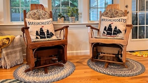 Two rocking chairs with 'Massachusetts' pillows, placed on patterned rugs in a room with large windows and a view of trees. - 4BD/2BA. Tranquil Cape Getaway for family  (Barnstable)