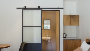 A modern hotel room with a bed, a desk, a chair, a sliding door, a sink, and a cabinet. - Eleven (Daylesford)