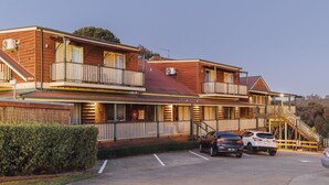 A two-story hotel with a balcony on the second floor, a covered outdoor seating area, and a parking lot with several cars. - Eleven (Daylesford)