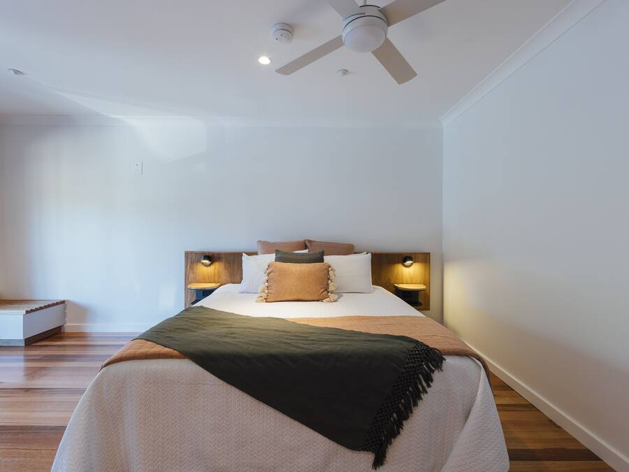 Ein modernes Schlafzimmer mit einem Bett, Nachttischlampen, einem Deckenventilator und einer Holzbank.