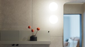 A bathroom vanity with a mirror, a vase with flowers, and two wall-mounted lights. - Eleven (Daylesford)