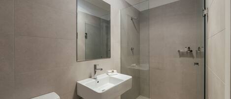 A modern bathroom with a glass shower enclosure, a white sink, and a toilet.