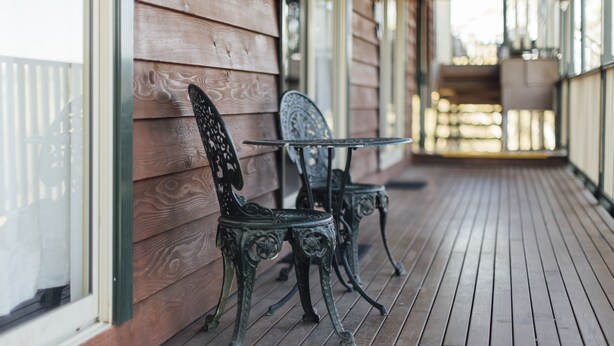 A wooden porch with two ornate metal chairs and a small table. - Eleven (Daylesford)