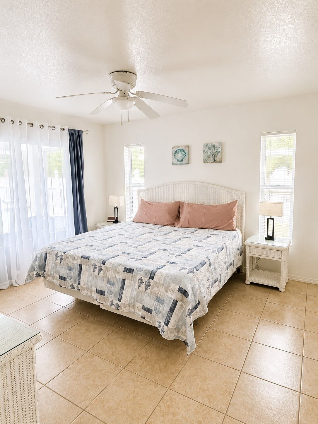A bedroom with a bed, a ceiling fan, a nightstand, and a window with curtains.
