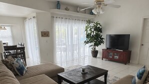 A living room with a sofa set, a coffee table, a TV on a stand, a ceiling fan, and a potted plant. - CHARMING FLORIDA GETAWAY 3BDR HOME WITH A POOL (Rotonda West)