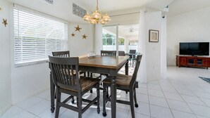 A dining area with a wooden table and chairs, a chandelier, and a television in the background. - CHARMING FLORIDA GETAWAY 3BDR HOME WITH A POOL (Rotonda West)
