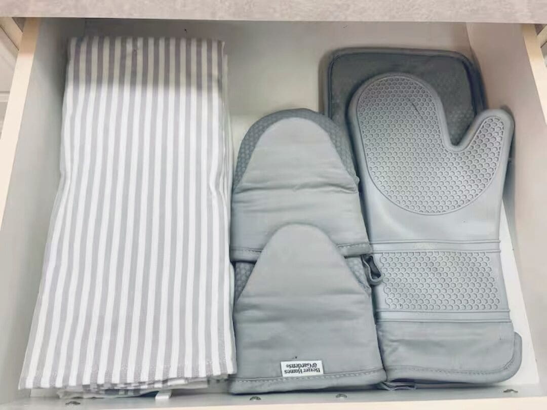 Eine Schublade mit Stoffmuster, zwei graue Topflappen und ein Topflappen in Grau mit strukturierter Grifffläche.