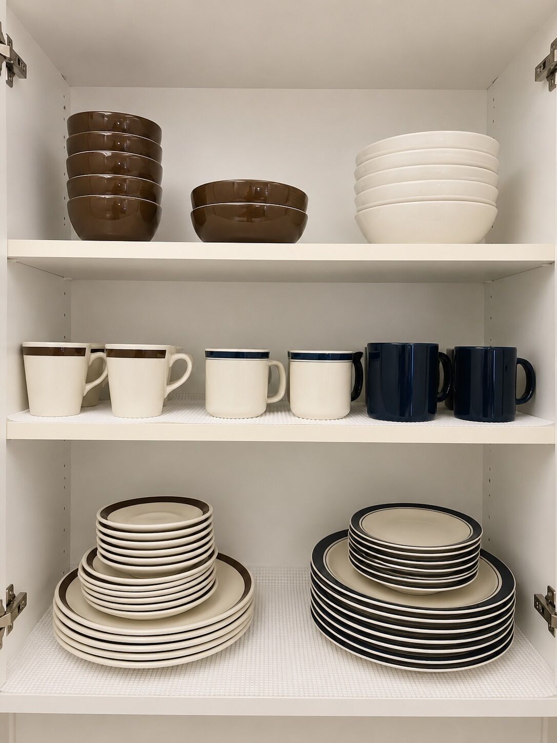 A kitchen cabinet with shelves containing stacked bowls, mugs, and plates.