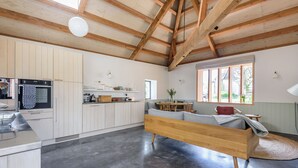 Eine moderne Küche mit weißen Schränken, einem eingebauten Ofen und einem Essbereich mit grauem Sofa und Holztisch.