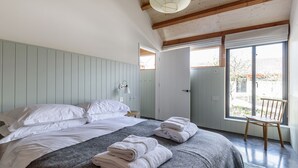 Ein ordentlich bezogenes Bett mit weißen Leinen, einer grauen Musterdecke und gefalteten Handtüchern.