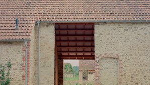 Un edificio con techo de tejas, fachada de ladrillo y un gran acceso abierto que da a un sendero.