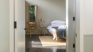 Un pasillo que conduce a un dormitorio con cama, una silla, una mesita y una lámpara colgante.