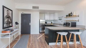 A modern kitchen with a central island, white cabinetry, and a small bar area with stools. - Music Row Retreat with Pool and Free Parking, Walk to Bars! (Nashville)