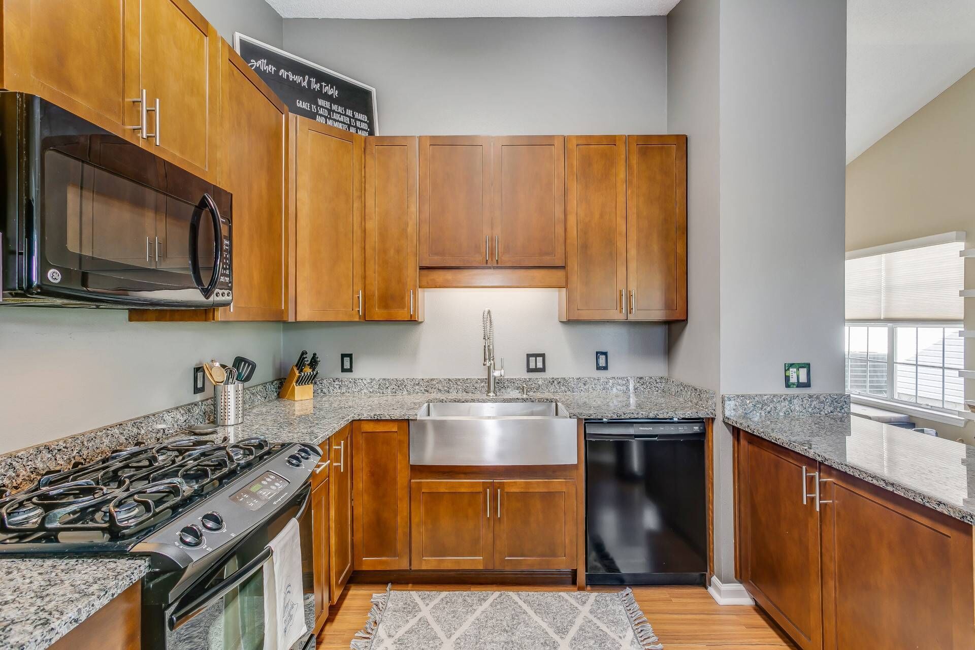 A modern kitchen with wooden cabinets, a stainless steel sink, a dishwasher, a microwave, and a gas stove.