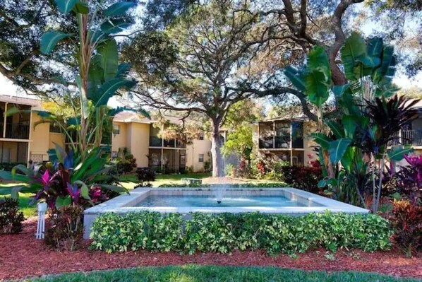 A courtyard with a central fountain, surrounded by lush greenery and large trees.