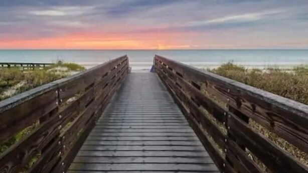 Un muelle de madera que lleva a una playa con un atardecer de fondo.