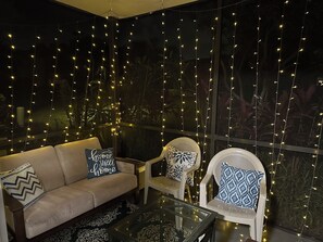 A cozy seating area with a sofa, two chairs, and a glass table, decorated with string lights.