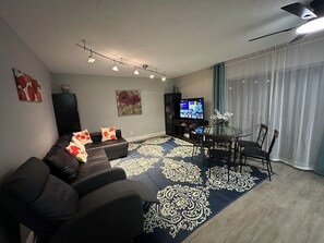 A living room with a sofa, a television, a dining table with chairs, and a patterned rug.