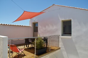 A balcony with a red shade sail, a potted plant, and outdoor furniture.