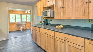 Una cocina con armarios de madera, un microondas y una zona de comedor con mesa y sillas.