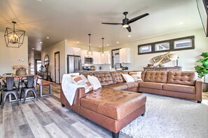 Una sala de estar amplia con un sofá seccional de cuero marrón, un comedor con mesa y sillas de madera, y una cocina con armarios blancos y electrodomésticos modernos.