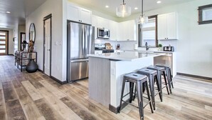 A modern kitchen with white cabinets, stainless steel appliances, and a central island with bar stools. - Modern Bozeman Family Townhome w/ Hot Tub! (Bozeman)