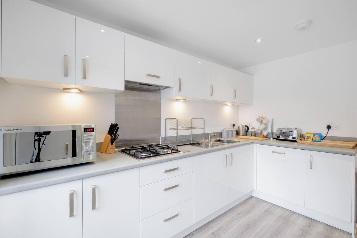 A modern kitchen with white cabinets, a built-in microwave, a gas stove, and a sink.