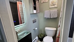 A compact bathroom with a glass sink, a toilet, and a shower area. - Beautiful Studio Suite #4 (Loa)