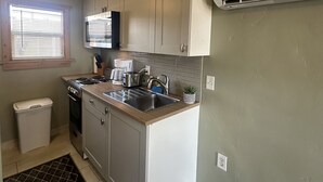 A compact kitchen with a stove, sink, and microwave. There is a trash can and a small rug on the floor. - Beautiful Studio Suite #4 (Loa)