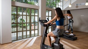 Een sportschool met grote ramen, trainingsapparatuur en uitzicht op groen.