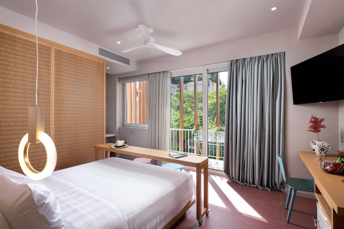 A modern hotel room with a bed, desk, and balcony with curtains.