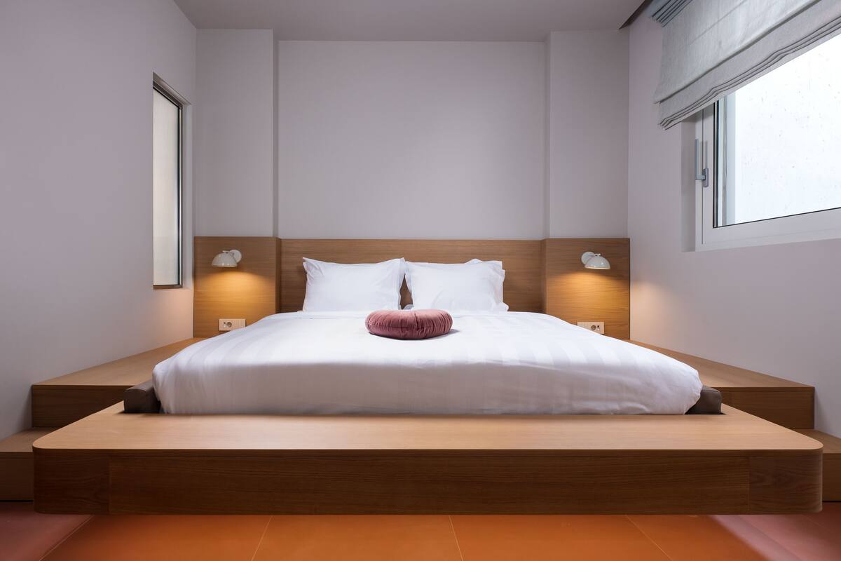 A modern bedroom with a wooden platform bed, white bedding, and two wall-mounted lamps.