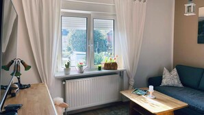 A cozy living room with a wooden table, a sofa, and a window with curtains.