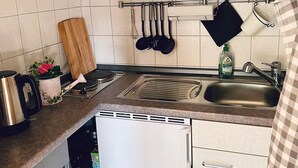 A kitchen with a stainless steel sink, a white dishwasher, and a hanging pot rack with various kitchen utensils.