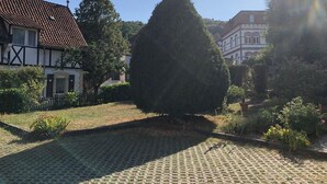 A courtyard with a paved area, a large conical tree, and traditional buildings with a tiled roof.