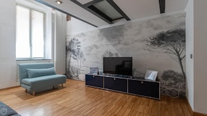 A modern living room with a sofa, a flat-screen TV on a black entertainment unit, and a wall with a nature-themed mural. - Italianway - Frisi 8 (Milan)