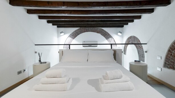 A modern bedroom with a large bed, white linens, and a brick archway. - Italianway - Frisi 8 (Milan)
