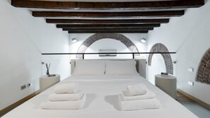 A modern bedroom with a large bed, white linens, and a brick archway. - Italianway - Frisi 8 (Milan)
