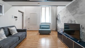 A modern living room with a grey sofa, a blue armchair, a flat-screen TV, and a decorative wall with a 'WELCOME TO MILAN' sign. - Italianway - Frisi 8 (Milan)