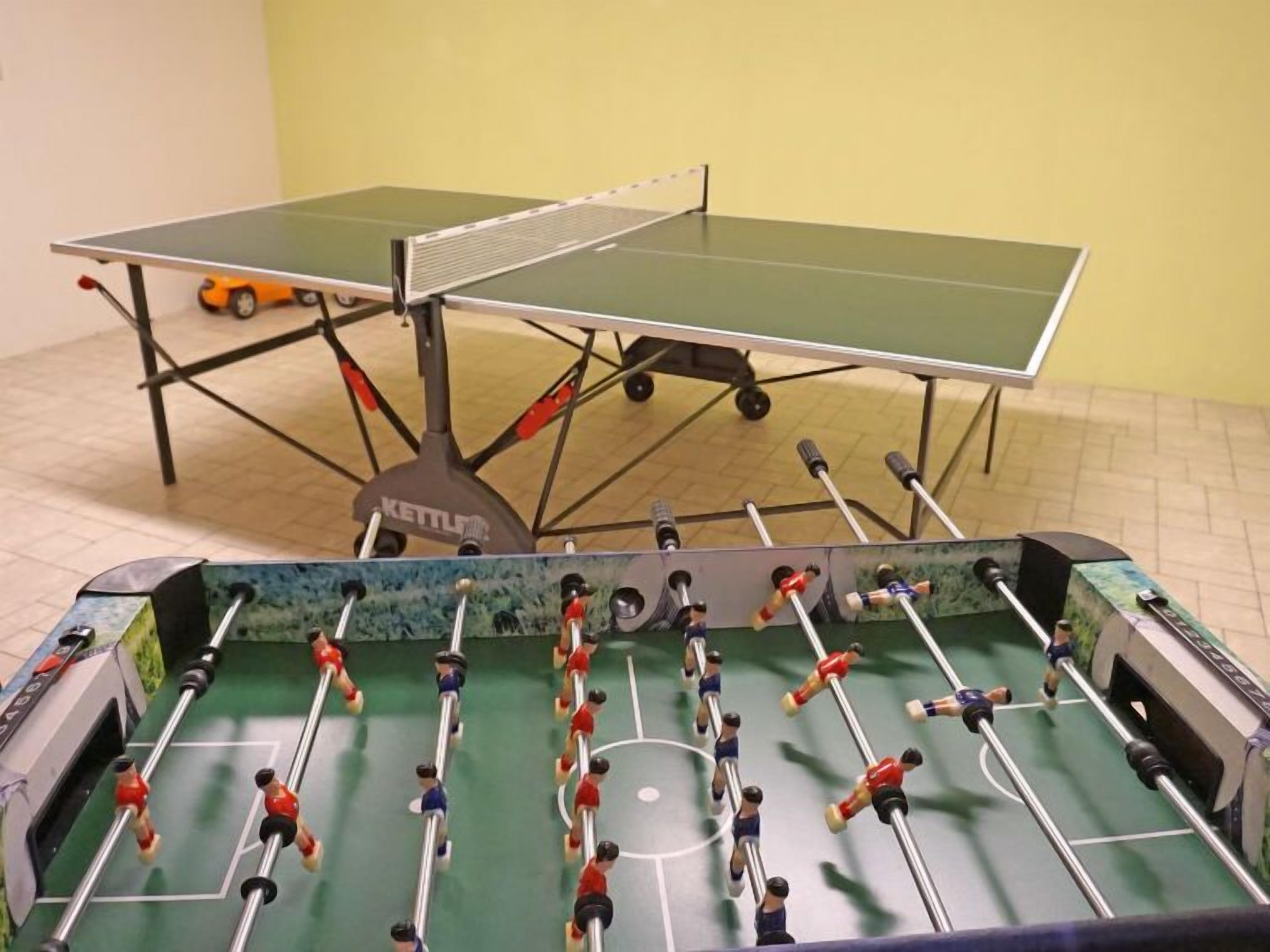 A foosball table with a green playing surface and metal rods, set against a yellow wall.