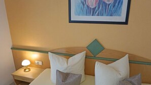 Ein Hotelzimmer mit Bett, Kissen, einem Nachttisch mit Lampe und einem Bild an der Wand.