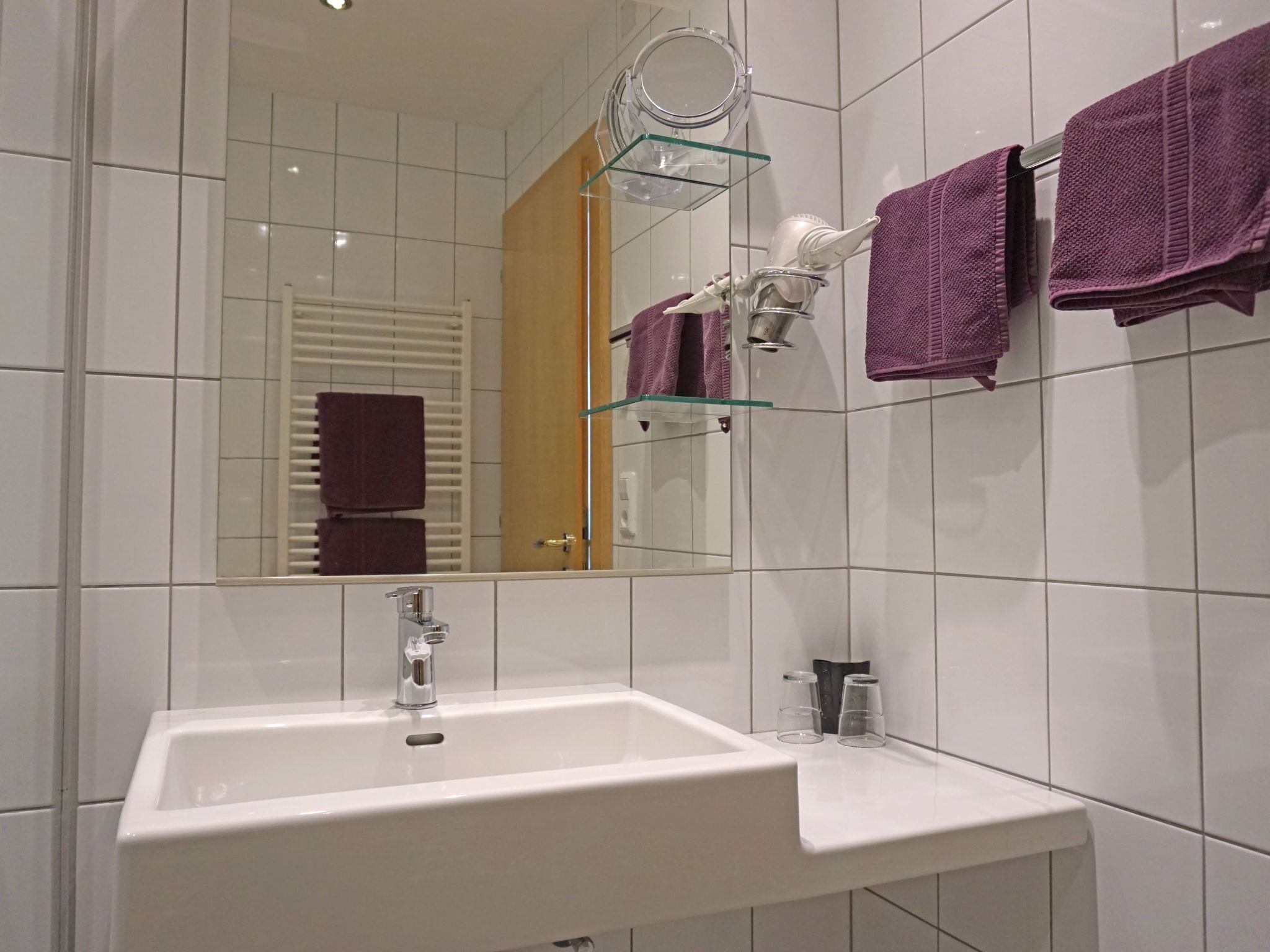 A bathroom with a white sink, a mirror, and two purple towels hanging on the wall.