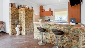 Une cuisine moderne avec un mur d’accent en pierre, un coin bar avec des tabourets et un téléviseur à écran plat fixé au mur.