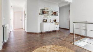 Un salon spacieux et moderne, doté d’un parquet, d’une console blanche et d’une table basse en verre.